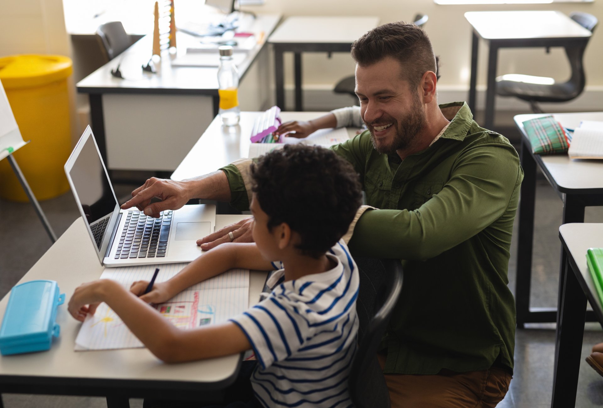 Young school teacher helping boy with study on laptop in