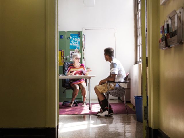 Principal talking with teenage boy while sitting in office